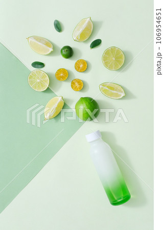 On a pastel paper background, a gradient bottle decorated with slices of lime and kumquat. Creative background for advertising cosmetics product with ingredient from natural 106954651