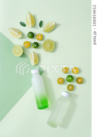 Scene for advertising product with ingredient from natural essential from lime and kumquat. Slices of lime and kumquat decorated with empty bottles on pastel background 106954652