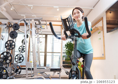 スポーツジムのエアロバイクで運動する女性（健康・ダイエット） 106955123