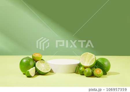 Against the green background, a podium in white color is displayed with piles of kumquats and limes. Against the green background, a podium in white color is displayed with piles of kumquats and limes. 106957359