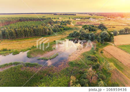 Beautiful sunset in the countryside in summer with the blazing sky. Rural landscape in the evening. Aerial view of brook, village, and arable fields. Panoramic view Beautiful sunset in the countryside in summer with the blazing sky. Rural landscape in the evening. Aerial view of brook, village, and arable fields. Panoramic view 106959436