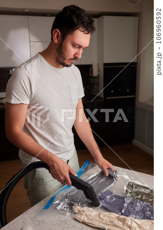 The girl pumps out air with a vacuum cleaner from a vacuum bag with clothes. The concept of storage and transportation of clothing, things. Space saving seal bag. 106960592