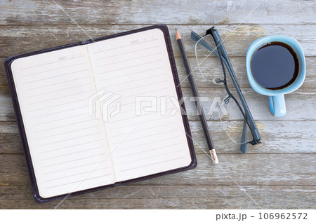 Blank paper notebook,glasses,pencil and cup of coffee on brown wooden table background. 106962572