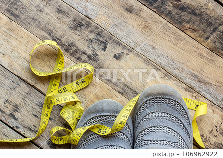 Yellow measuring tape and sport shoes on wooden table 106962922