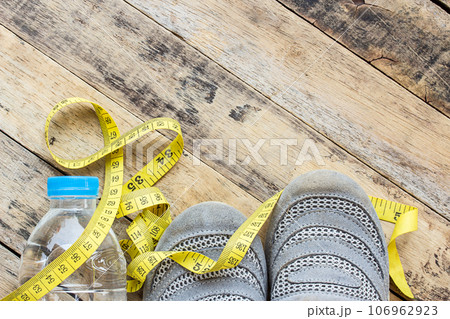 Yellow measuring tape, sport shoes and water on wooden table 106962923