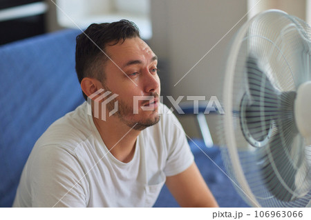 Young man relaxing under the air fan at home 106963066