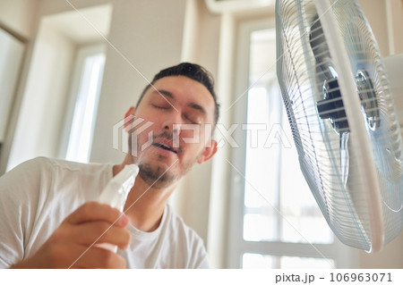 Young man relaxing under the air fan at home Young man relaxing under the air fan at home 106963071