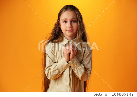 Little girl begging looking at viewer against yellow backgorund in studio Little girl begging looking at viewer against yellow backgorund in studio 106965148