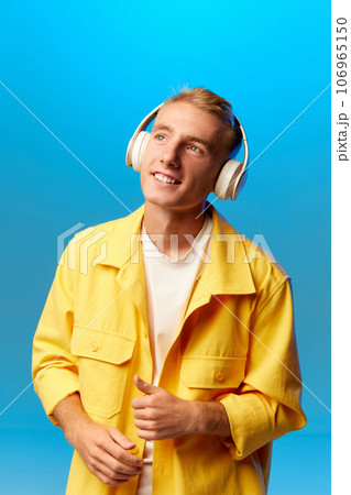 Portrait of young handsome guy, student in bright fashion outfit and headphones looking away isolated on blue background blue background. 106965150