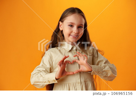 Happy little girl making heart shape by hands on yellow background 106965156
