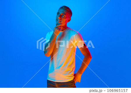 Portrait of young man, student on blue studio background in neon light, filter. Handsome, dreaming male model in casual style. 106965157