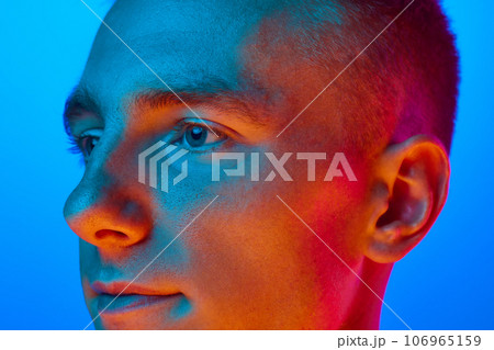 Close Up side view portrait of young handsome calm guy, student isolated on blue background in red neon light, filter. Confident, serious man. Close Up side view portrait of young handsome calm guy, student isolated on blue background in red neon light, filter. Confident, serious man. 106965159