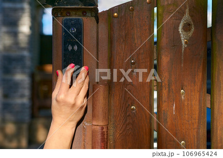 Woman's hand pressing a doorbell on a wooden fence in the garden 106965424