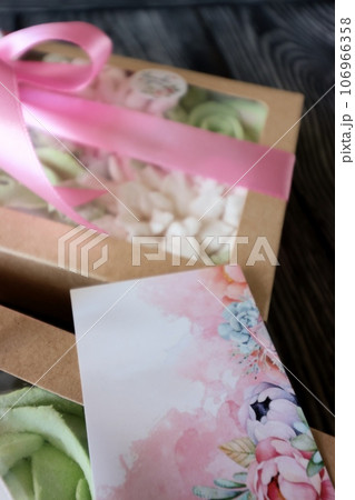 Two boxes with marshmallows. Zephyr flowers. Homemade marshmallows in a paper gift box. The box is tied with a ribbon tied into a bow. Label for the text. Near the congratulatory postcard. Close-up. Two boxes with marshmallows. Zephyr flowers. Homemade marshmallows in a paper gift box. The box is tied with a ribbon tied into a bow. Label for the text. Near the congratulatory postcard. Close-up. 106966358