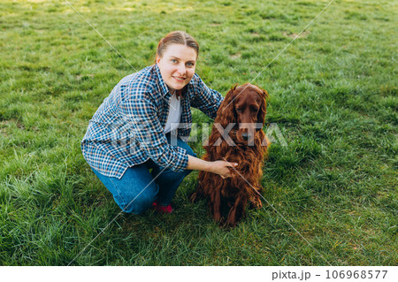 Human and a dog. Woman and her friend dog on the straw field background. Beautiful Irish Setter dog is sitting in grass. Domestic animals concept 106968577