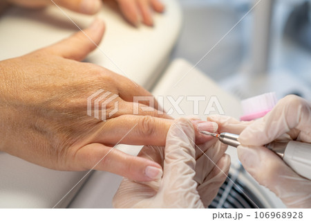Nail care procedure in a beauty salon. Female hands and tools for manicure, process of performing manicure in beauty salon. Gloved hands of a skilled manicurist cutting cuticles. Concept spa body care 106968928