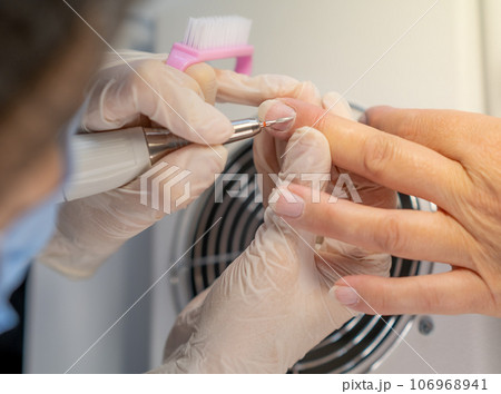 Nail care procedure in a beauty salon. Female hands and tools for manicure, process of performing manicure in beauty salon. Gloved hands of a skilled manicurist cutting cuticles. Concept spa body care 106968941