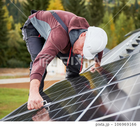 Man technician mounting photovoltaic solar panels on roof of house. Engineer in helmet installing solar module system with help of hex key. Concept of alternative, renewable energy. 106969166