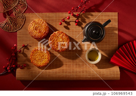 Bamboo blinds featured a tea set in black color and three mooncakes with elegant patterns. Tree branches decorated. Mid Autumn Festival minimalist design 106969543