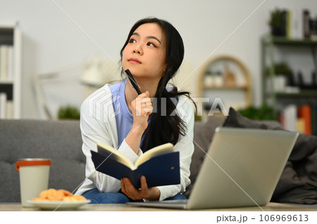 Thoughtful young female freelancer thinking, solving problem and using laptop in living room 106969613