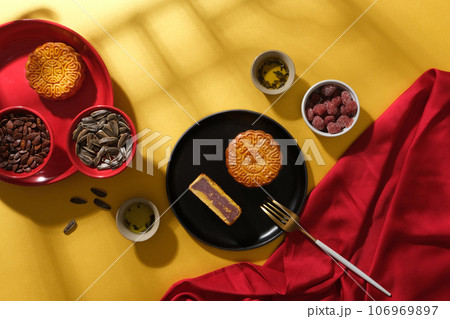 Creative layout of tea table party decorated with appetizing mooncakes, nuts and jams. A red silk cloth makes the whole photo stand out. Scene for advertising. Chinese mid-autumn festival 106969897