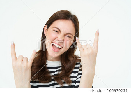 Let it rock. Excited, laughing young woman, showing heavy metal, horns gesture and smiling, having fun, expressing positivity and joy, standing over white background 106970231