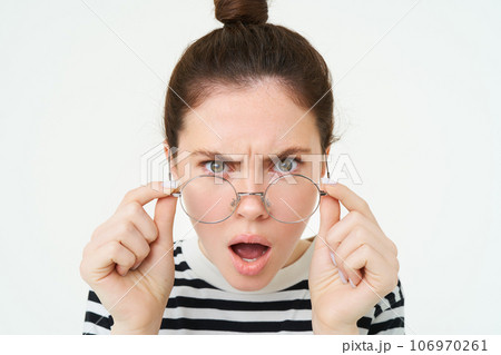 Close up of shocked, insulted young woman, frowning and looking offended, reading smth offensive and upsetting, takes off glasses, stands over white background 106970261