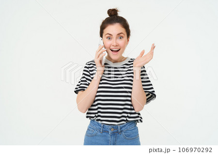 Portrait of girl answers phone call, reacts surprise, stands over white background. Communication and lifestyle concept Portrait of girl answers phone call, reacts surprise, stands over white background. Communication and lifestyle concept 106970292
