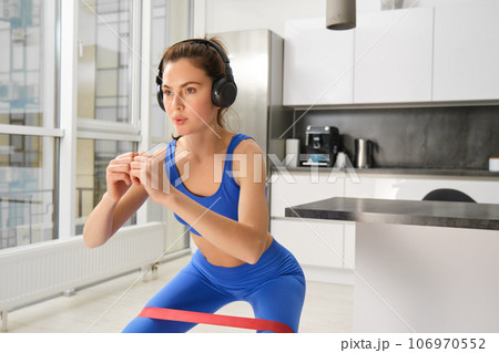 Portrait of woman doing squats with elastic resistance band, looking focused during workout, doing exercises at home 106970552