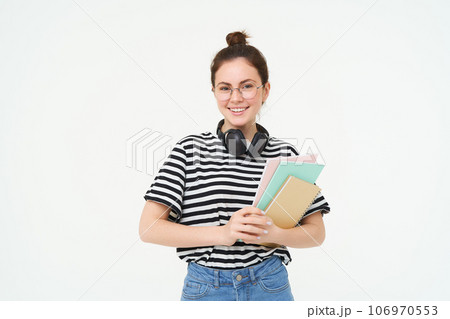 Image of young woman, tutor with books and notebooks, wearing headphones over her neck, isolated on white background. Student lifestyle concept 106970553