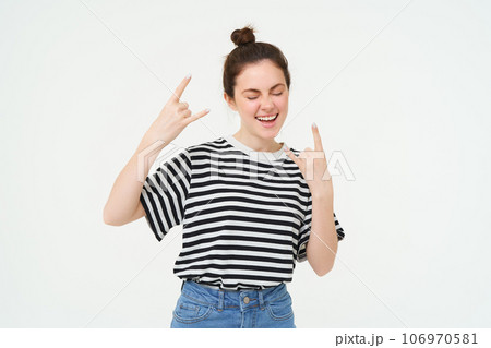 Portrait of attractive, carefree woman dancing, showing heavy metal, rock on gesture, standing over white background 106970581