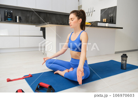 Image of beautiful woman doing training, workout from home in living room, practice yoga, sitting on floor and meditating 106970603