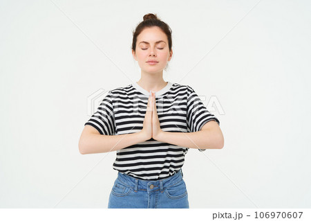 Portrait of young mindful woman meditating, holds hands clasped together, namaste gesture, practice yoga, standing over white background 106970607