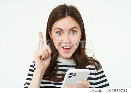Got an idea. Smiling woman, raises her finger and holds smartphone, suggests something, makes eureka gesture, has a solution, white background 106970751