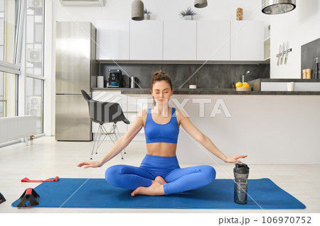 Portrait of calm and relaxed young woman, sitting on yoga rabber mat, concentrating on breathing exercises, doing mindful training at home 106970752