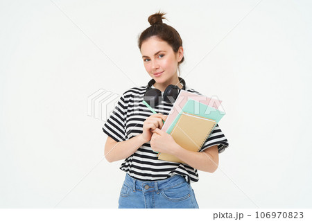 Image of young woman, tutor with books and notebooks, wearing headphones over her neck, isolated on white background. Student lifestyle concept 106970823