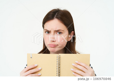 Portrait of girl looking puzzpled, perplxed face of woman, holding notebook, confused by something, standing over white background Portrait of girl looking puzzpled, perplxed face of woman, holding notebook, confused by something, standing over white background 106970846