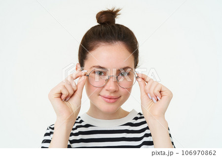 Close up portrait of smiling, attractive young woman wearing new eyewear, trying on glasses for vision, standing over white background 106970862