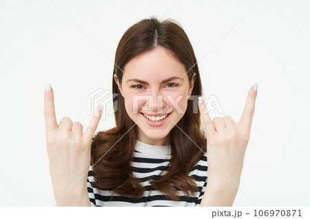 Close up portrait of excited young woman, rock n roll girl, showing heavy metal horn fingers and smiling, enjoys concert, having fun, standing isolated over white background Close up portrait of excited young woman, rock n roll girl, showing heavy metal horn fingers and smiling, enjoys concert, having fun, standing isolated over white background 106970871