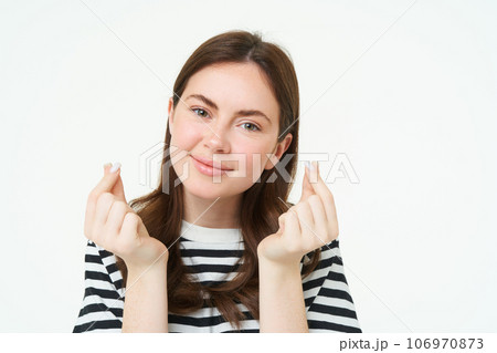 Portrait of beautiful young woman shows finger hearts sign, love and care, likes smth, stands over white studio background 106970873