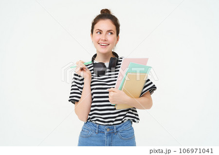 Portrait of young woman, student with notebooks and earphones on her neck, posing for college advertisement, white background Portrait of young woman, student with notebooks and earphones on her neck, posing for college advertisement, white background 106971041