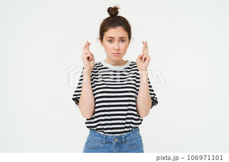 High hopes. Young woman cross fingers, makes wish, anticipates something, stands over white background 106971101