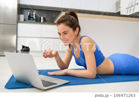 Image of young fitness girl talking online on laptop, video chats, laying on floor rubber mat, doing exercises, discuss workout training, yoga from home 106971263