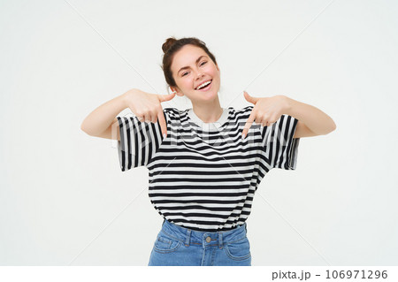 Enthusiastic girl points fingers down, shows advertisement, promo banner below, stands over white background Enthusiastic girl points fingers down, shows advertisement, promo banner below, stands over white background 106971296