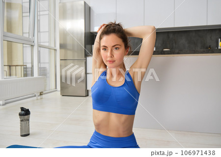 Portrait of young fitness woman, stretching her body, doing yoga exercises on mat in living room, workout at home, wearing blue activewear Portrait of young fitness woman, stretching her body, doing yoga exercises on mat in living room, workout at home, wearing blue activewear 106971438