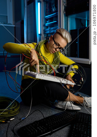 Young woman IT technician wrapped in wire repairing keyboard 106971800
