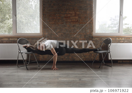 Man ballet dancer doing stretching performing split with two chairs 106971922