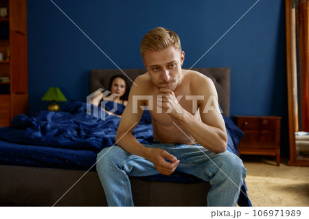 Frustrated upset man sitting on bed with woman on blurred background 106971989