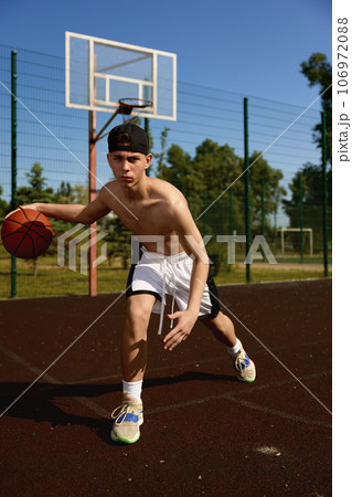 Active teenager basketball player practicing with ball on street court Active teenager basketball player practicing with ball on street court 106972088