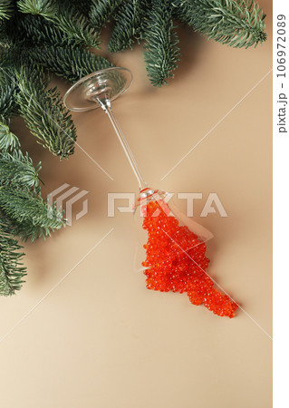 Red caviar splashed out of a glass wine glass. Spruce branches in the background. Salmon caviar. Delicacies. A festive snack. A useful omega. 106972089